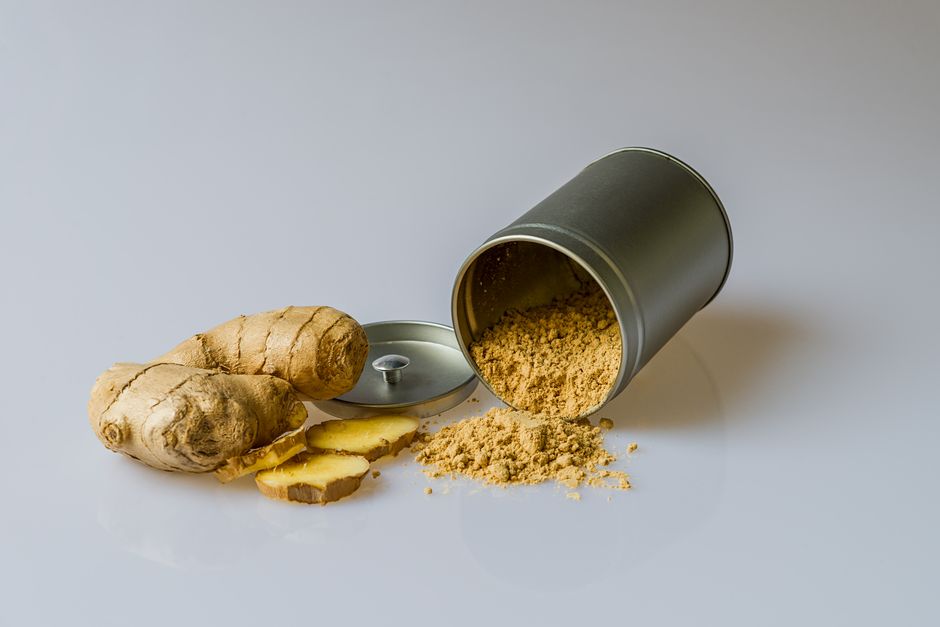 Ginger, Ground - Close-up of fresh ginger root with sliced pieces and ginger powder spilled from a metal container.