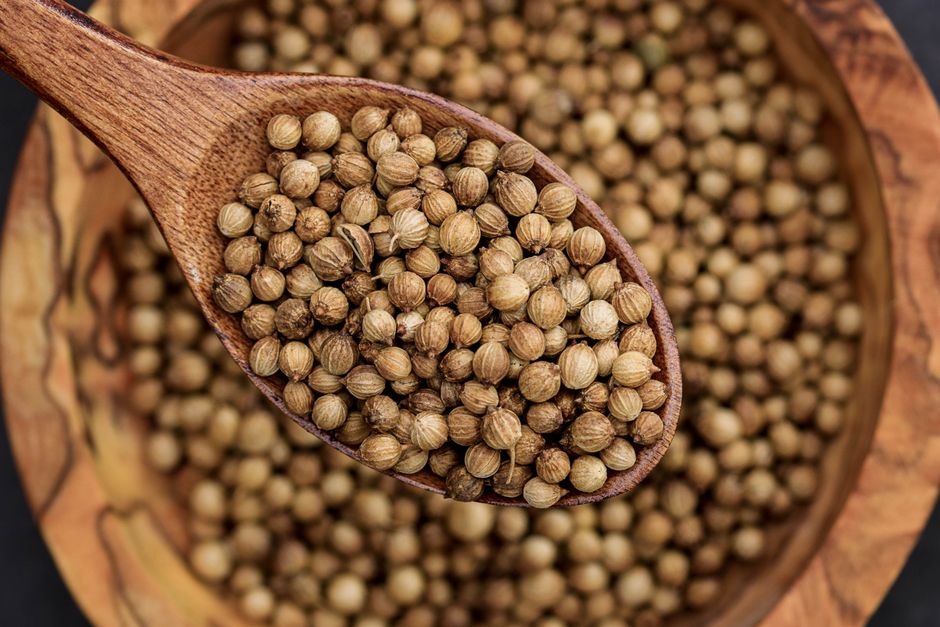 Coriander - Detailed view of coriander seeds in a wooden spoon, emphasizing texture.