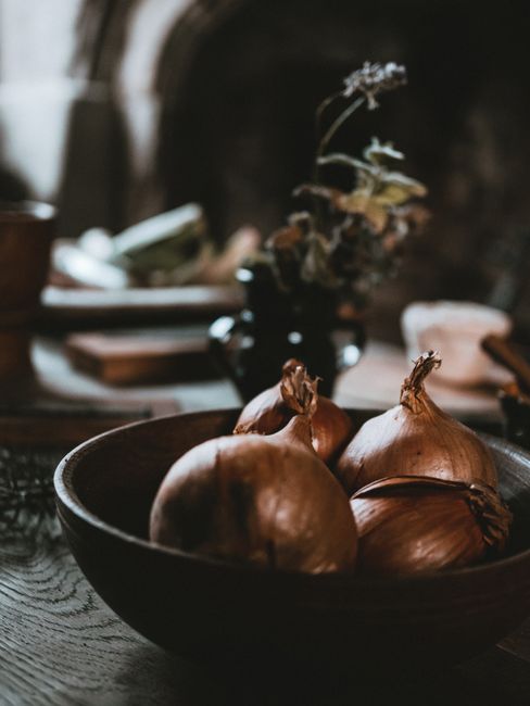 Onion Powder - Warm still life of onions in a wooden bowl on a rustic kitchen table.