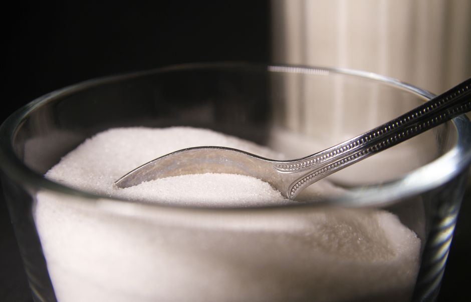 Sugar - Detailed shot of granulated sugar in a glass bowl featuring a spoon.