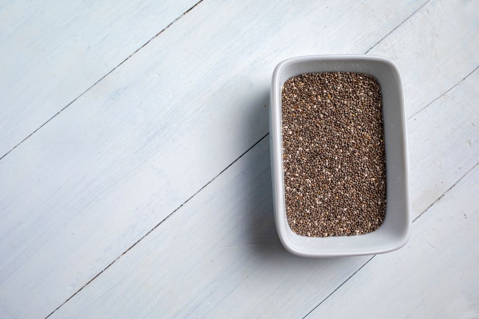 Chia Seeds - A close-up of chia seeds in a white bowl on a light wooden surface, showcasing a healthy food concept.