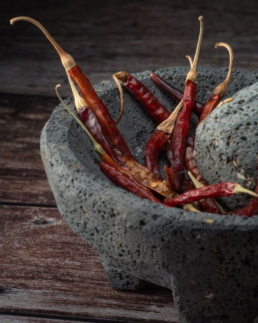Guajillo - Dried red chili peppers in a rustic stone mortar on a wooden table, perfect for spice enthusiasts.