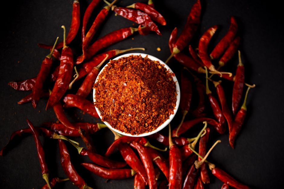 Chili Powder - Red chili powder and whole chilies on dark background, showcasing spice and flavor.