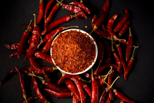 Chili Powder - Red chili powder and whole chilies on dark background, showcasing spice and flavor.