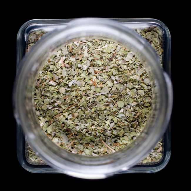 Marjoram - Herbs stored in a clear jar showcasing dried marjoram leaves from above.