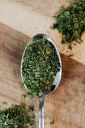 Oregano, Dry - A detailed view of dried oregano herbs on a spoon over a wooden surface, showcasing freshness and texture.