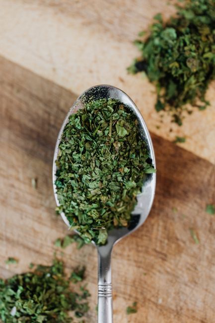 Oregano, Dry - A detailed view of dried oregano herbs on a spoon over a wooden surface, showcasing freshness and texture.