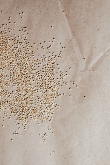 Quinoa - Overhead view of scattered organic quinoa seeds on textured brown paper background.