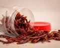 Puya - Vibrant dried red chili peppers spilling from a transparent jar with a red lid.