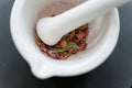 Safflower - A close-up view of dried herbal petals in a white mortar and pestle, creating a fragrant and aromatic setting.