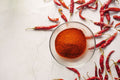 Cayenne Pepper - Bowl of vibrant chili powder surrounded by red chili peppers on a textured white background.